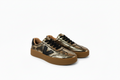 A pair of low-top sneakers featuring a metallic gold and bronze textured leather upper, black leather logo and laces, and a thick brown gum sole, shown on a white background.