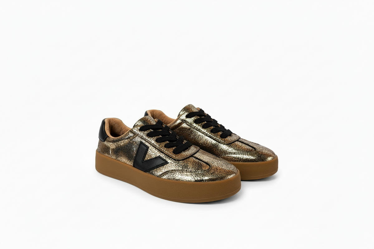A pair of low-top sneakers featuring a metallic gold and bronze textured leather upper, black leather logo and laces, and a thick brown gum sole, shown on a white background.