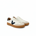 A pair of low-top sneakers in off-white leather and beige suede, featuring a prominent navy blue V logo on the side, cream laces, and a brown gum rubber sole.